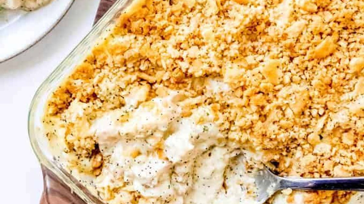 An image of a creamy poppy seed chicken casserole with some servings scooped out onto plates nearby.